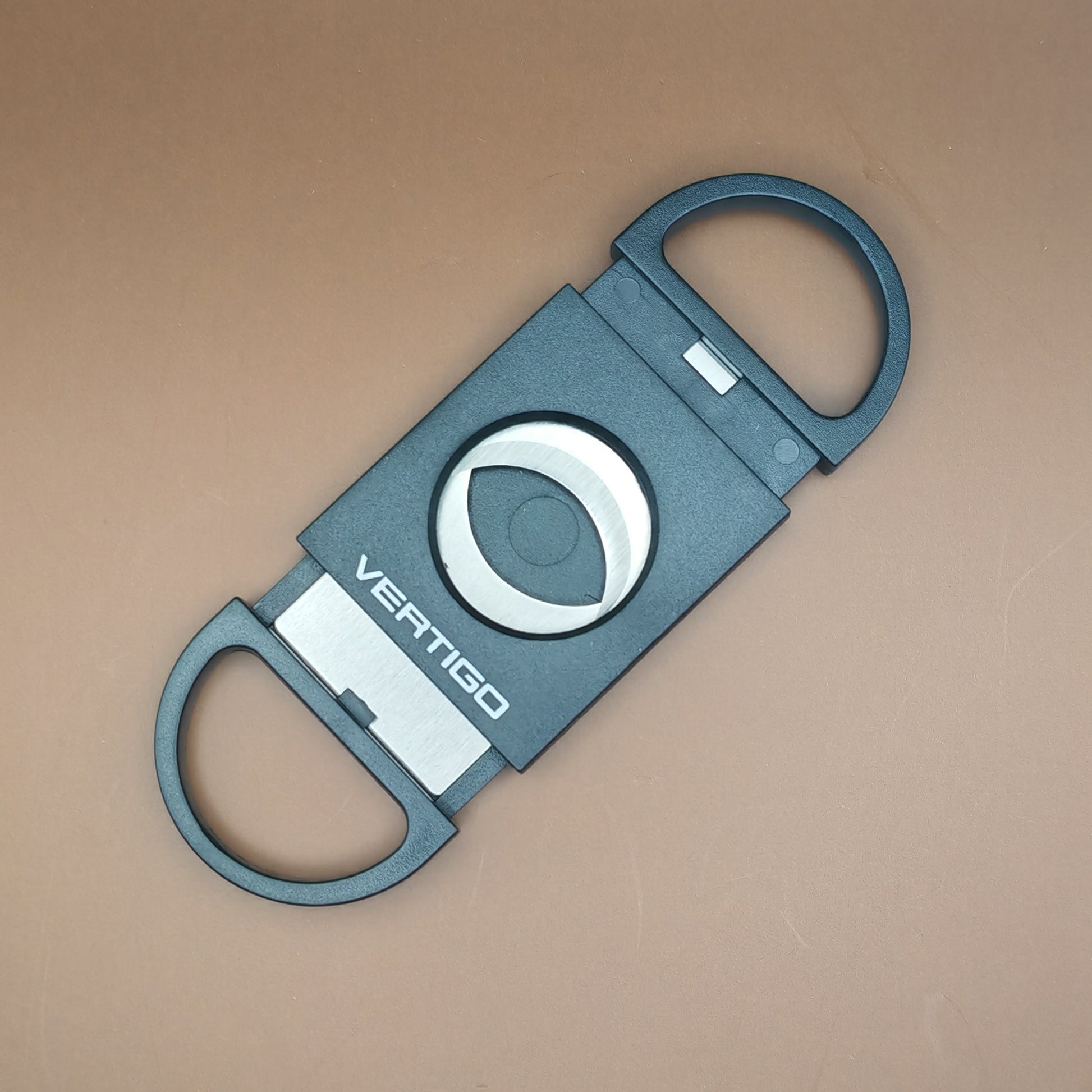 Black cigar cutter with 'VERTIGO' branding on a beige background