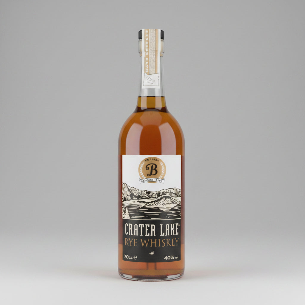 A bottle of Crater Lake Handcrafted American Rye Whiskey, showing the amber liquid inside a clear glass bottle with a white and black label.