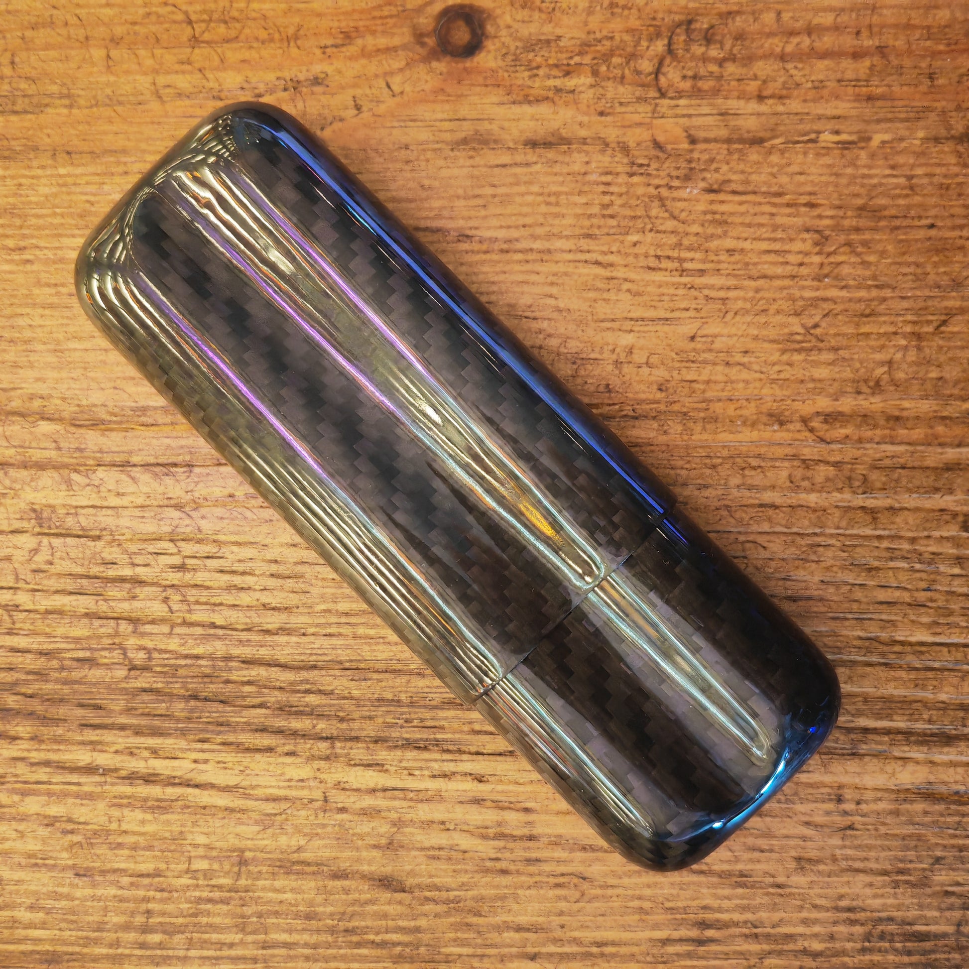 Carbon fiber cigar case with reflective surface on a wooden surface