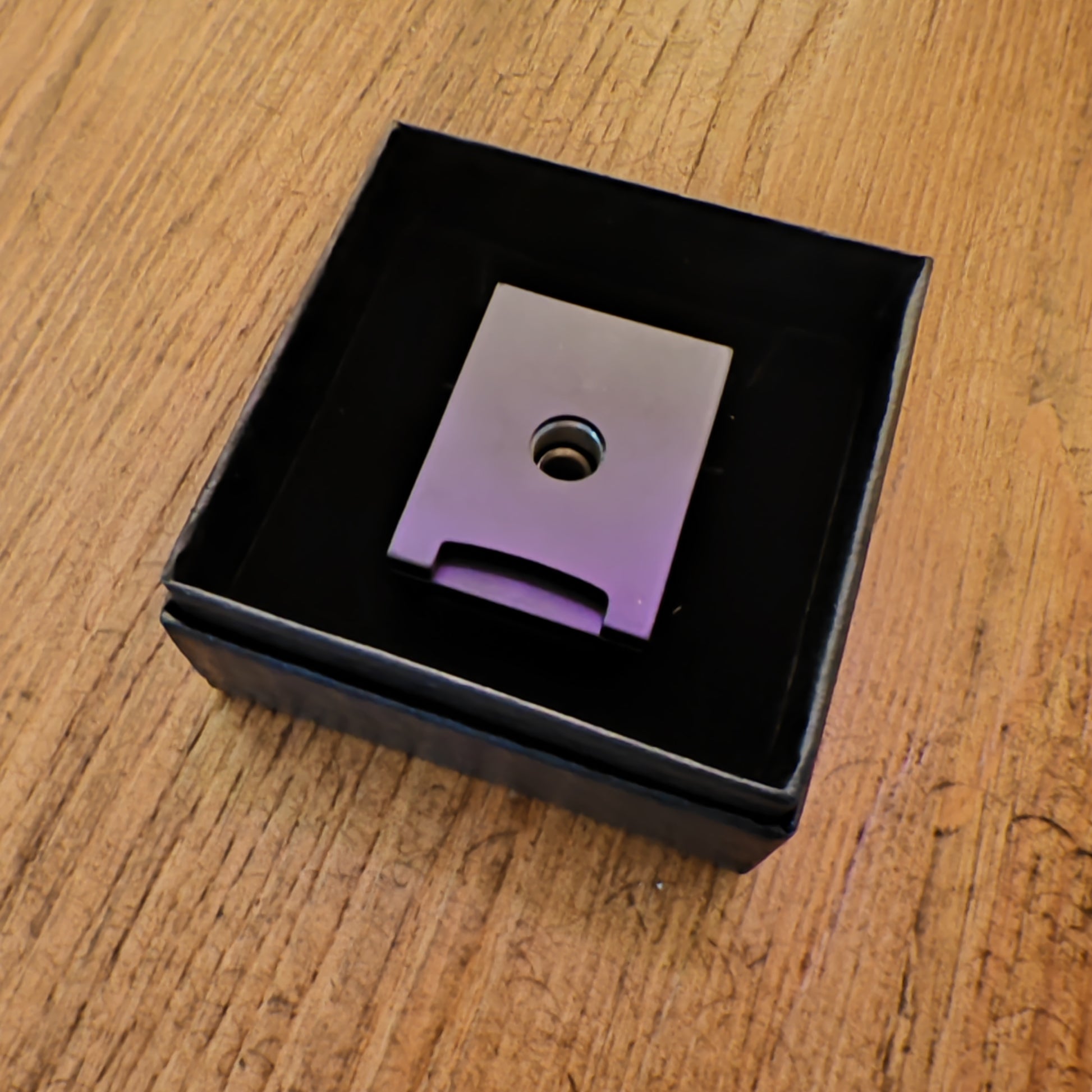 Metallic Cigar piercer with a central hole in a black box on a wooden surface