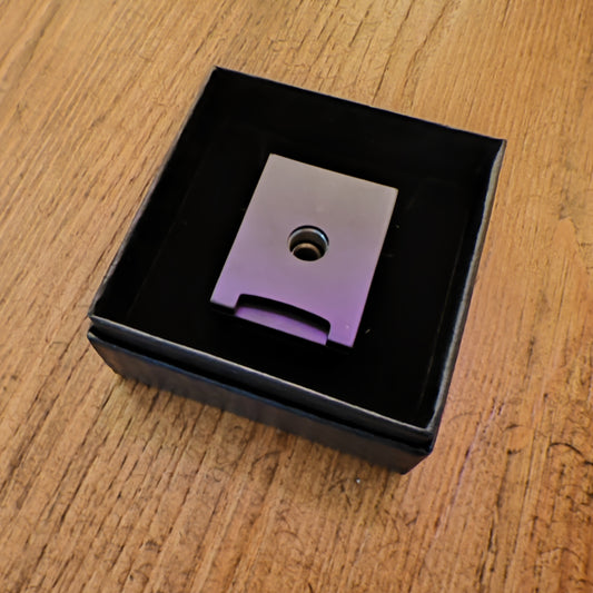 Metallic Cigar piercer with a central hole in a black box on a wooden surface