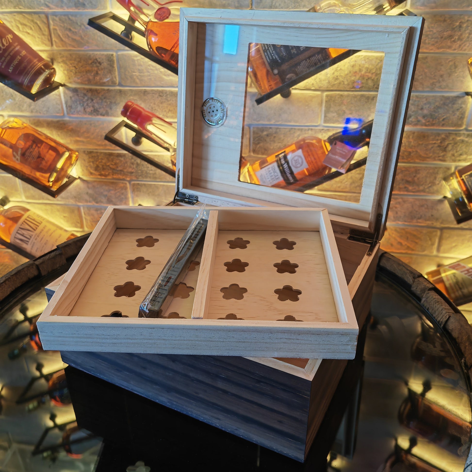 Wooden humidor with a mirror on top, surrounded by bottles against a brick wall.