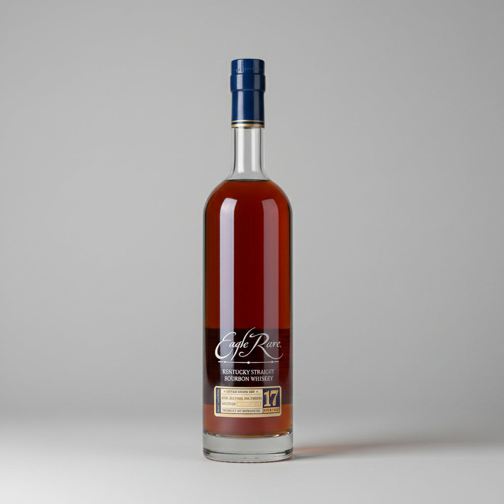 A bottle of Eagle Rare 17 Year Kentucky Straight Bourbon Whiskey stands on a wooden surface next to a small glass of the amber liquor, with a blurred barrel room background.