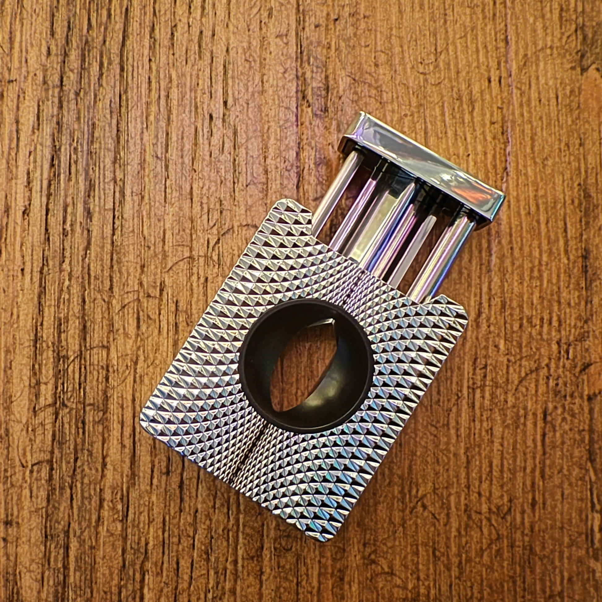 Metallic diamond-patterned cigar cutter on a wooden surface
