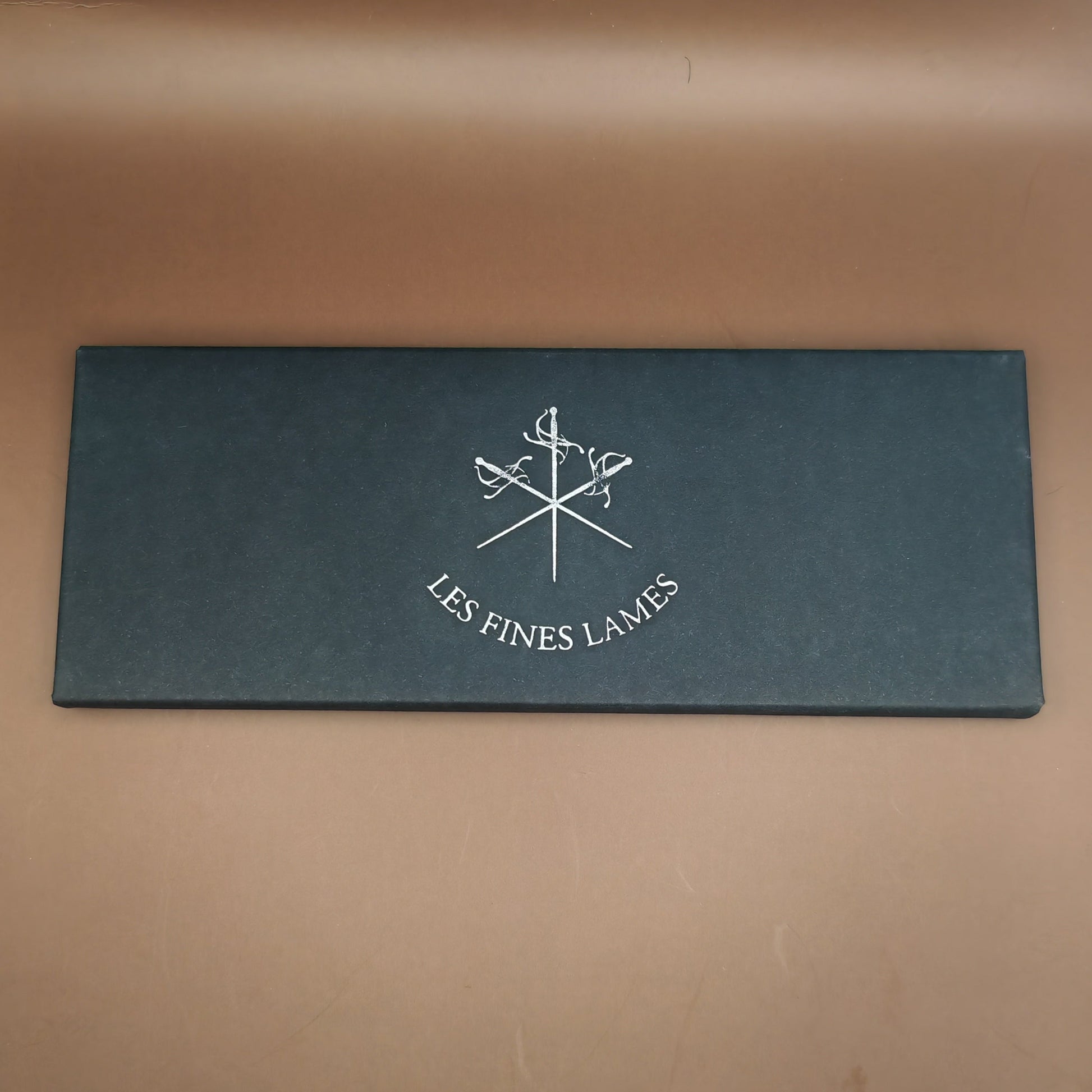 Black leather wallet with 'Les Fines Lames' logo on a brown leather background
