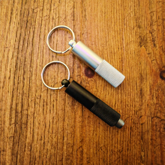 Two keychain cigar punch tools on a wooden surface