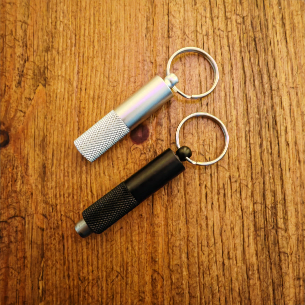 Two keychain cigar punch tools on a wooden surface