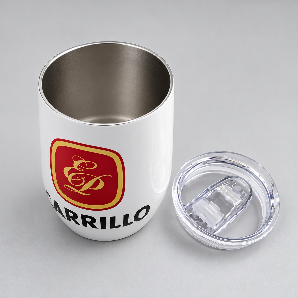 A white stainless steel tumbler with a clear lid, featuring the Carrillo logo in red and gold with the word 'CARRILLO' printed in black. The tumbler is shown next to its clear lid on a neutral gray background.