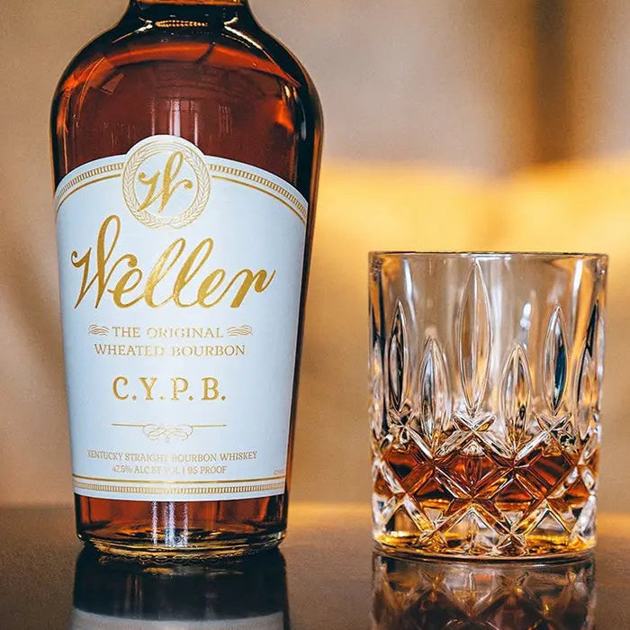 Weller CYPB whiskey bottle and glass on a reflective surface with a blurred background