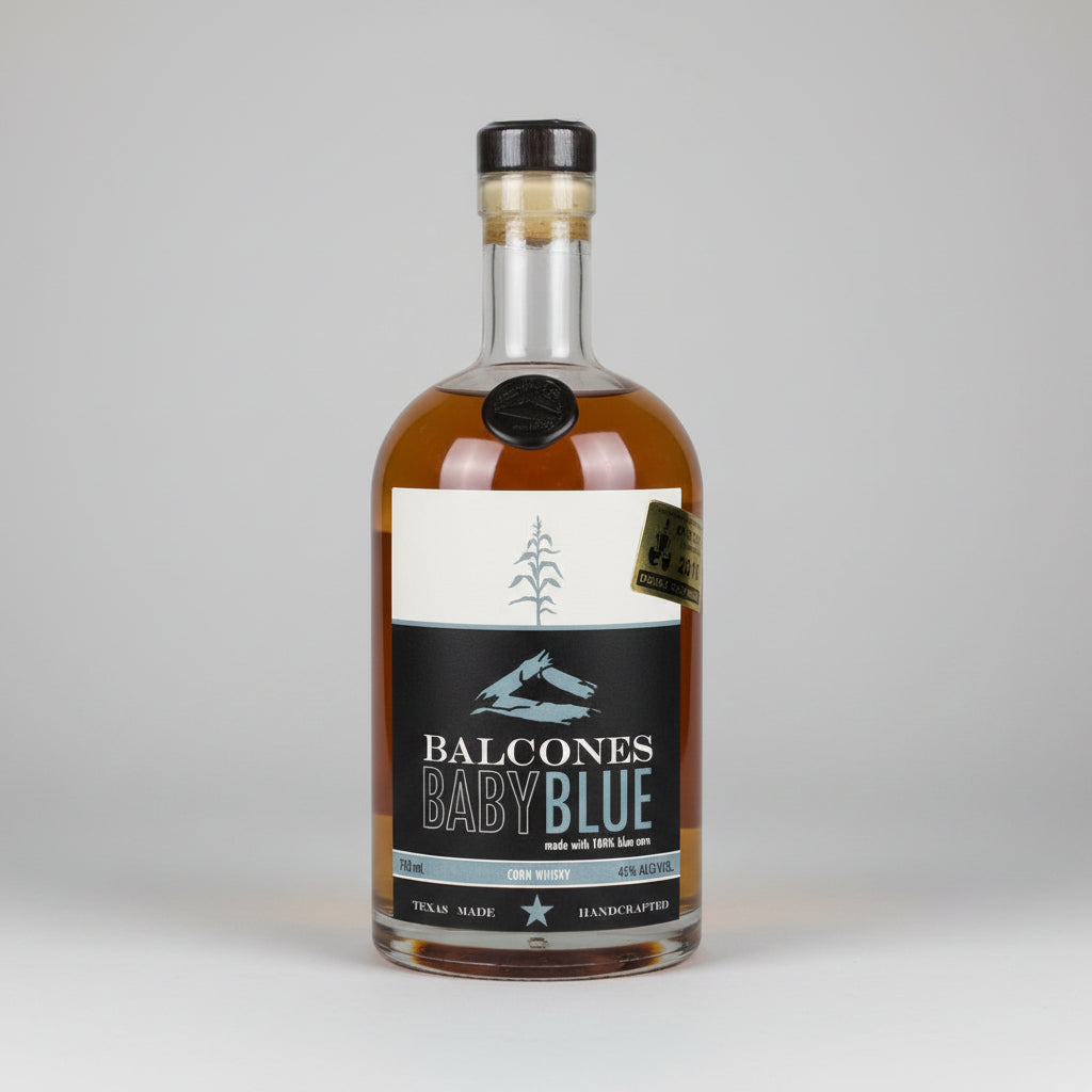 A bottle of Balcones Baby Blue bourbon whiskey against a white background, featuring a black and white label with a pine tree graphic.