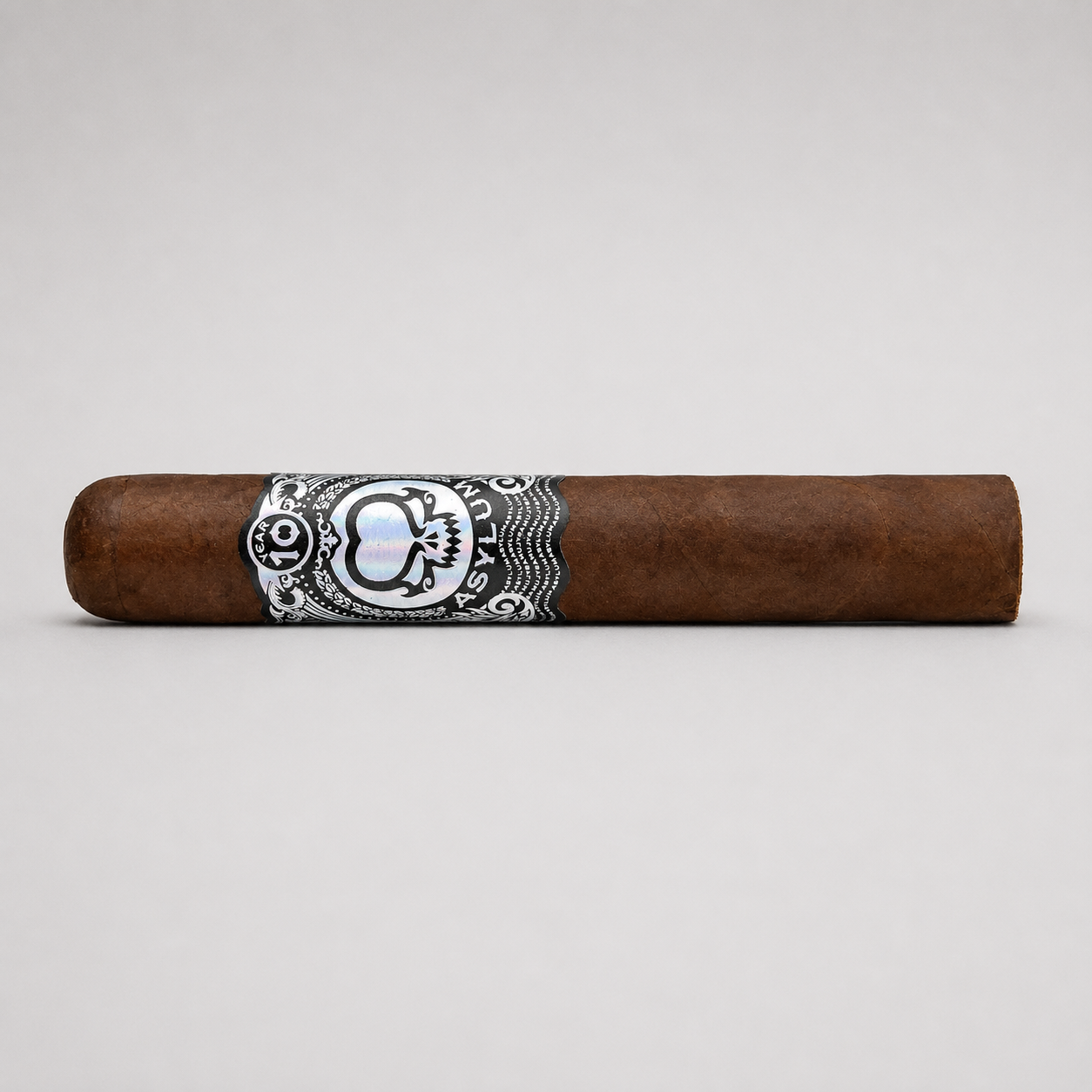 A single brown cigar with a detailed black, white, and silver band, photographed horizontally against a neutral light gray background.