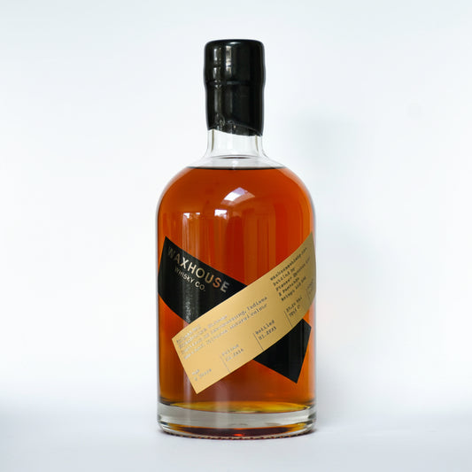 A bottle of Waxhouse Whiskey Co. AMERICAN RYE whisky, showing the amber liquid through a clear glass bottle with a black cap and a diagonal tan and black label.