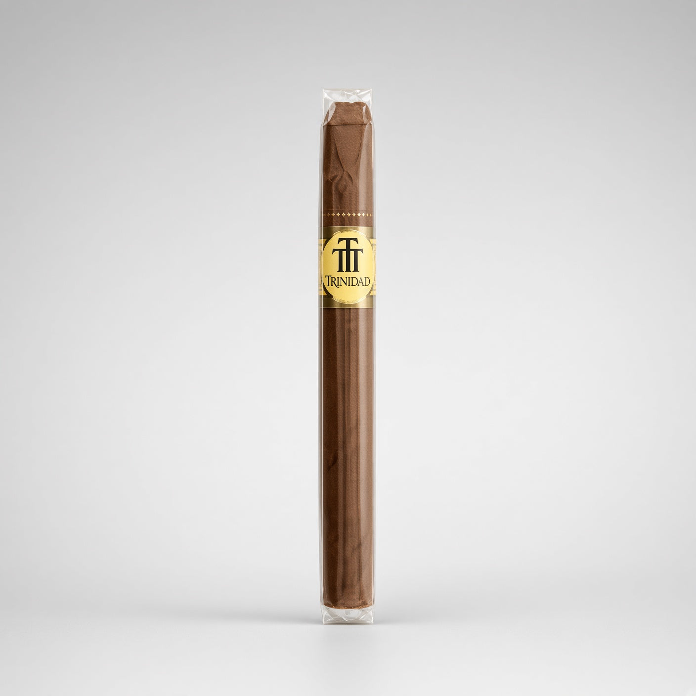 A single Trinidad cigar in its clear plastic wrapper, showing a dark brown wrapper body with a gold and black logo band, set against a light gray studio background.