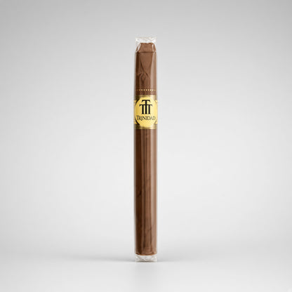 A single Trinidad cigar in its clear plastic wrapper, showing a dark brown wrapper body with a gold and black logo band, set against a light gray studio background.