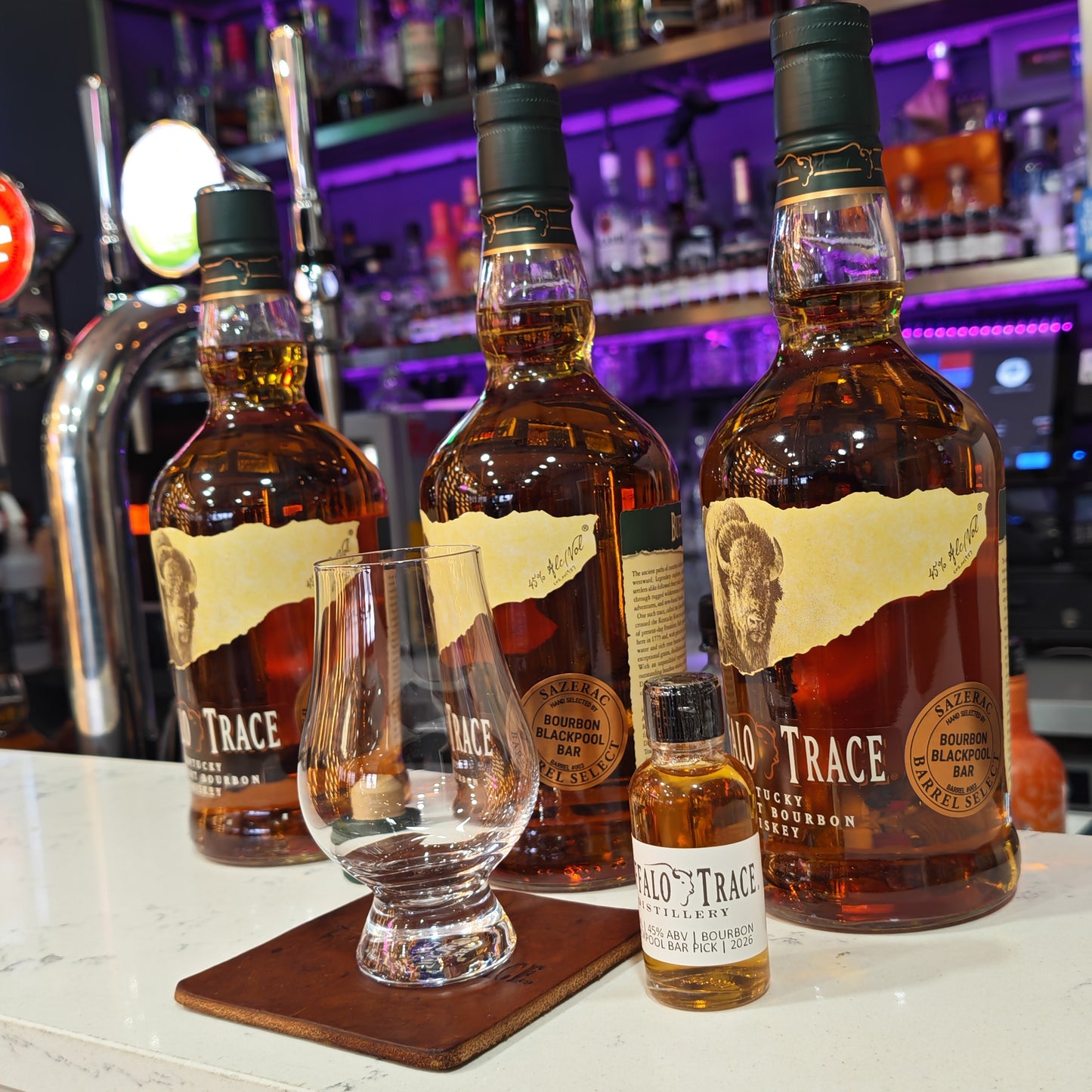 Three bottles of Buffalo Trace Single Barrel whiskey with a glass on a bar counter.