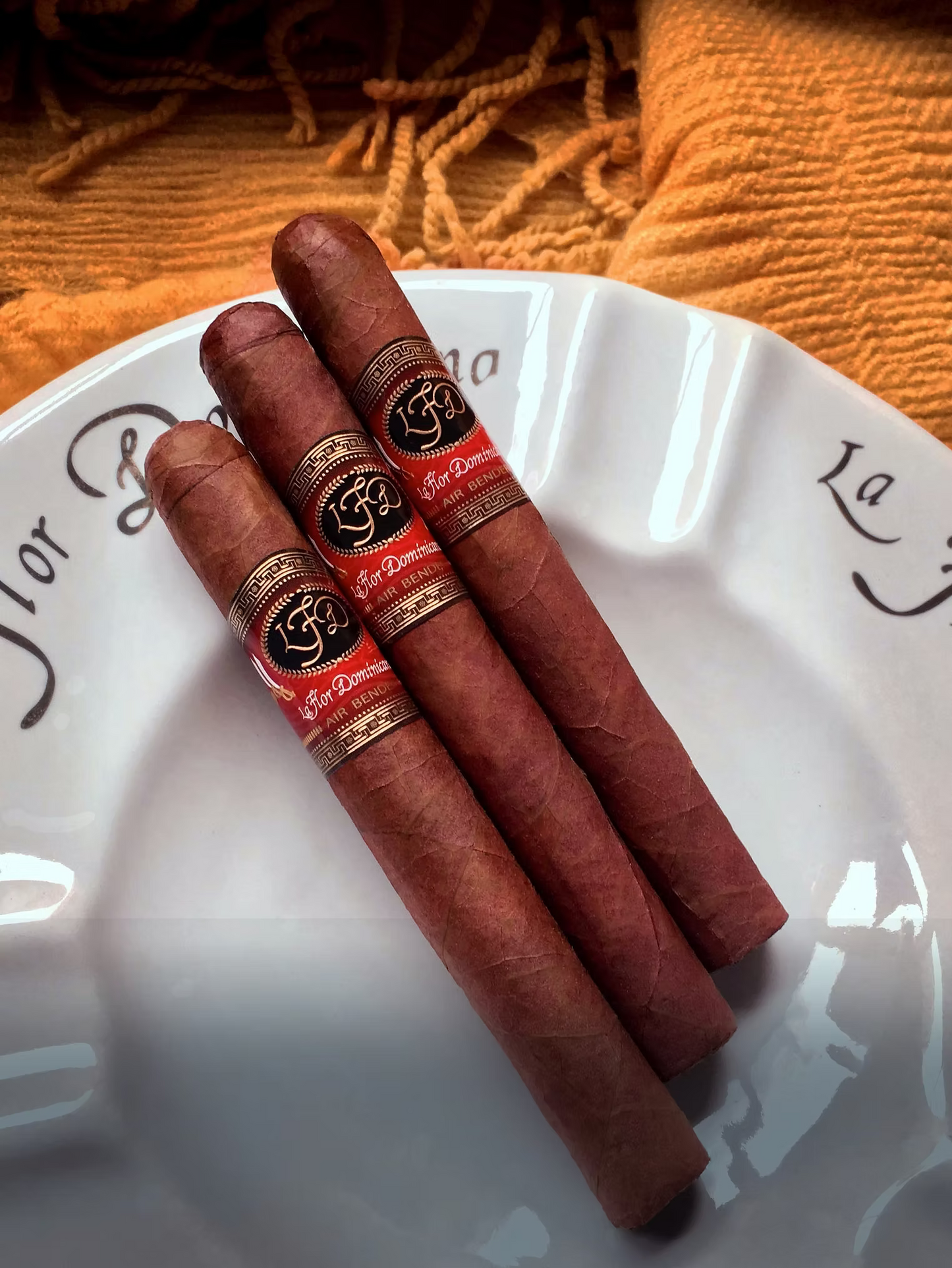 Three cigars with decorative bands on a white plate against an orange textured background