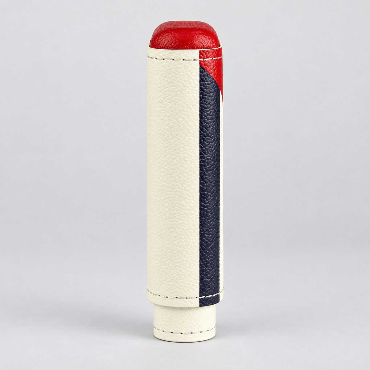 A cylindrical leather accessory with a cream-colored textured body, a dark navy blue vertical stripe, and a red top cap, photographed on a light gray background.