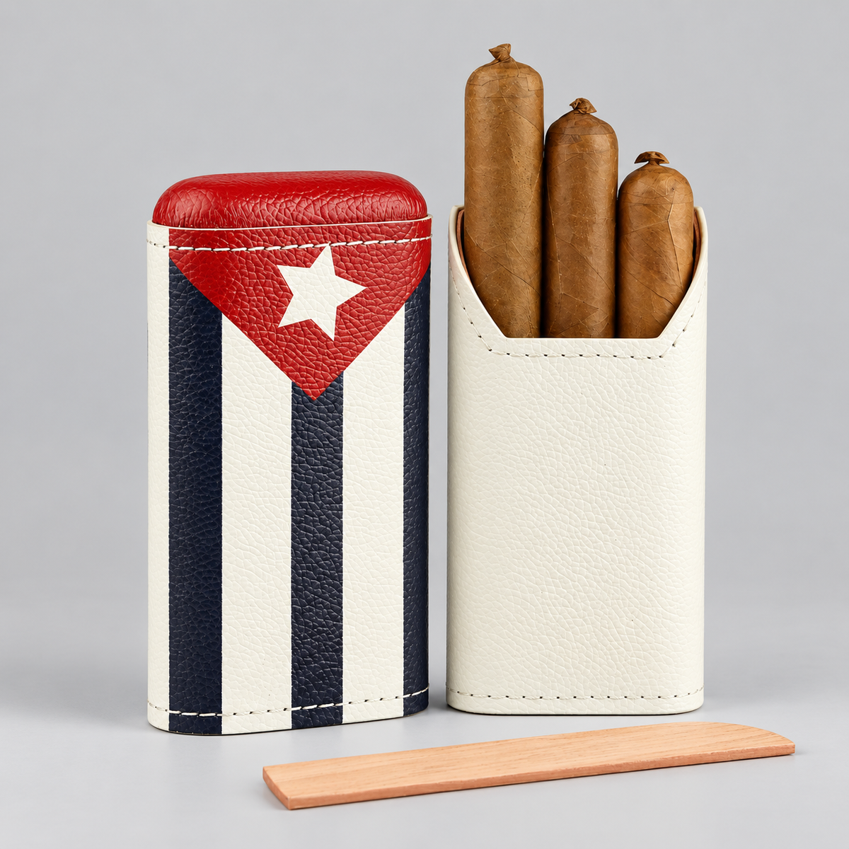 Two leather cigar cases on a light gray studio background, one closed with a Cuban flag design and one open holding three cigars, with a wooden stick in front.