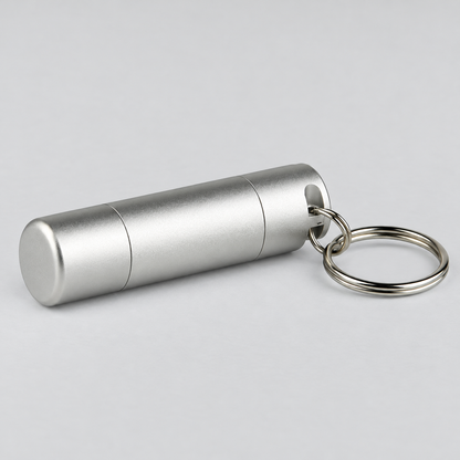 A silver aluminum cylindrical keychain container with a matching split key ring, shown on a neutral light gray background.