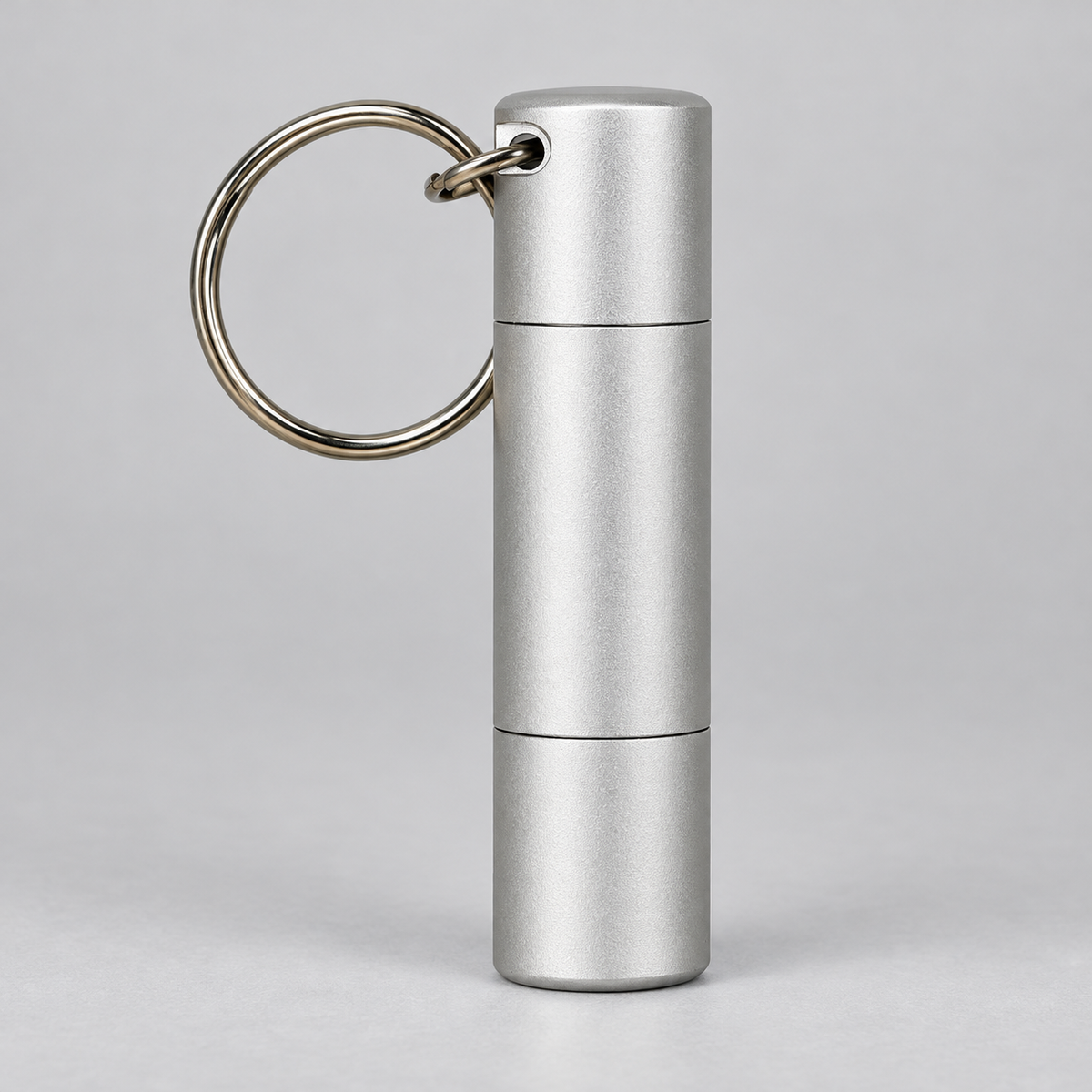 A silver metallic cylindrical keychain container with a split ring, shown on a neutral light gray background.