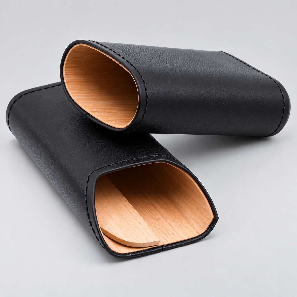 Two black leather watch strap cases with light wood interiors, arranged on a light gray background.