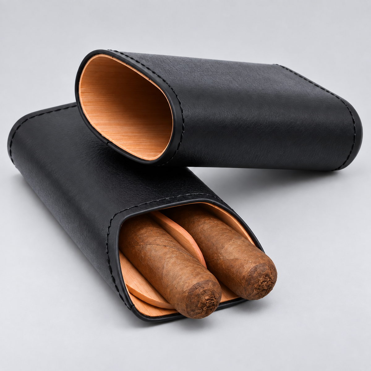 Two black leather cigar cases on a light gray background, one closed and one open showing two cigars inside with a light wood interior.