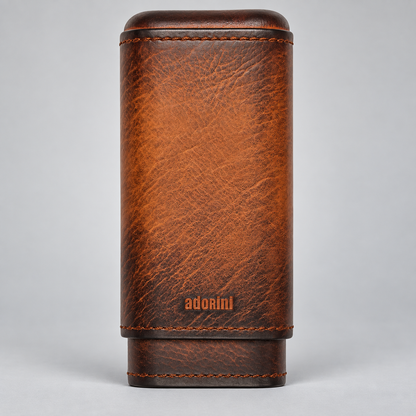 A brown textured leather cigar case with visible stitching and the brand name 'adorini' embossed near the bottom, photographed against a neutral gray background.