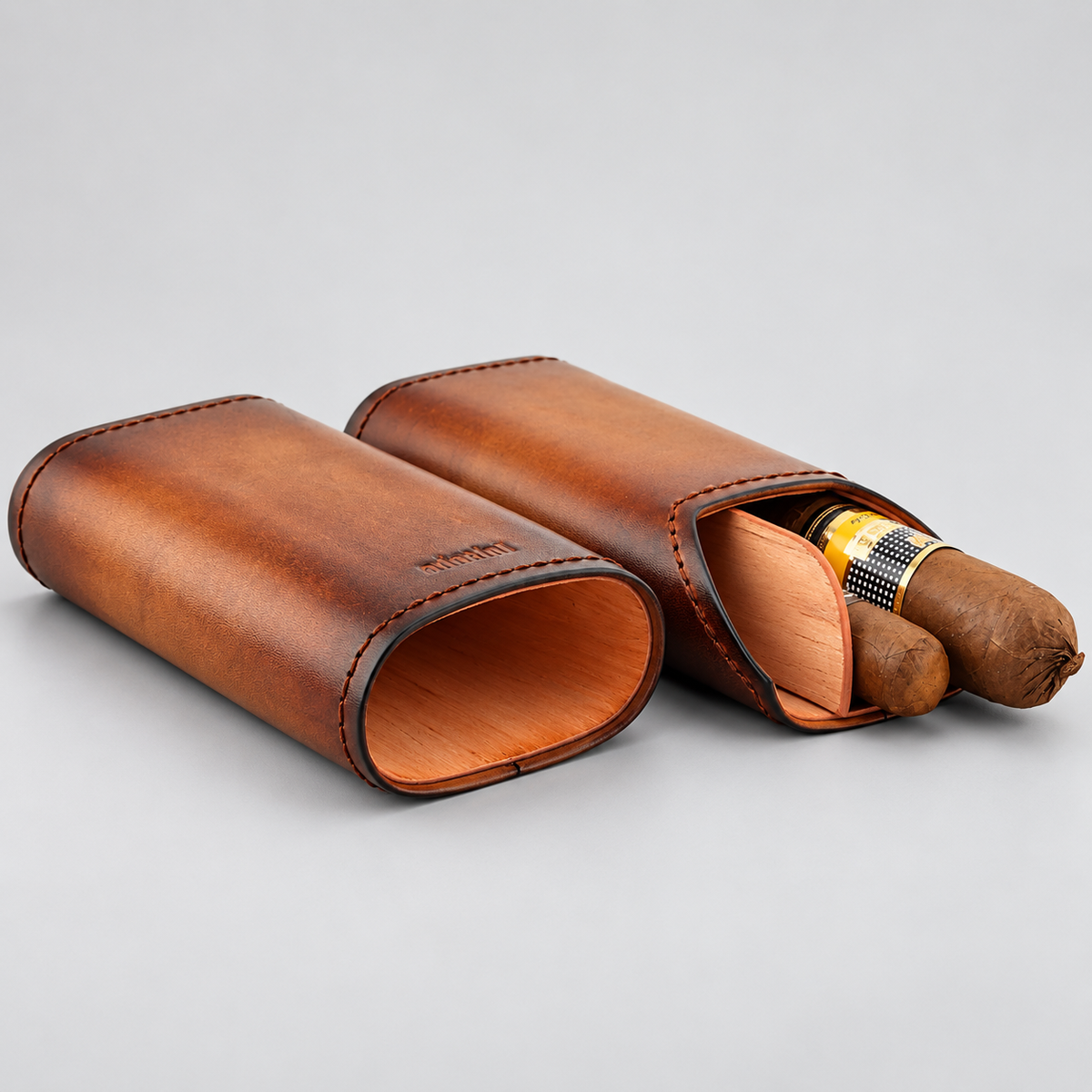 Two brown leather cigar cases on a light gray background, one closed and one open showing a cigar inside.