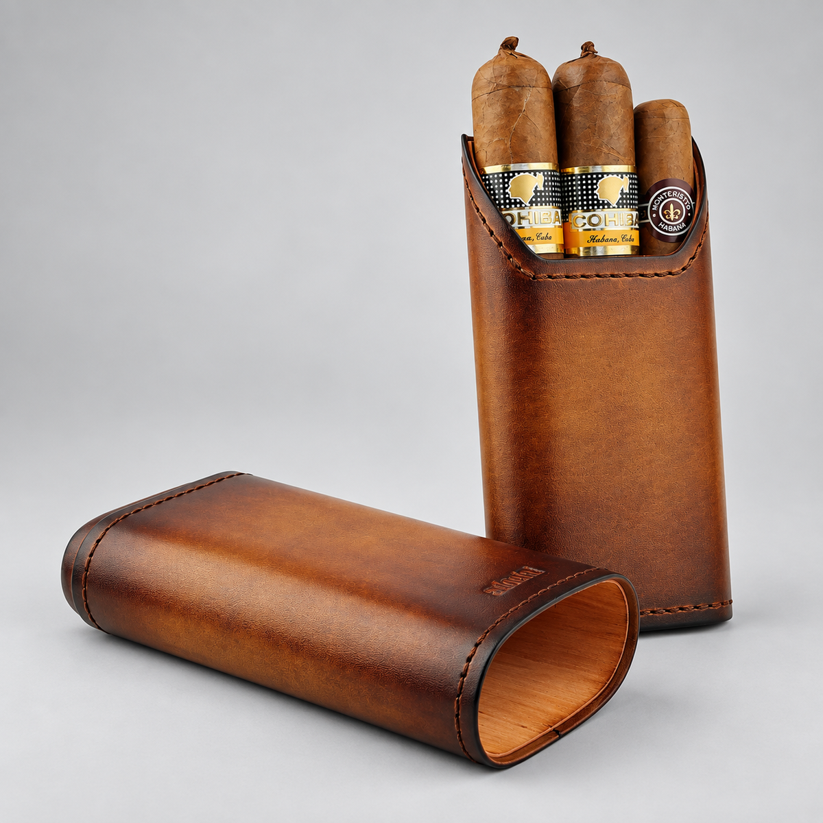 A brown leather cigar case shown open and closed on a light gray studio background, with three cigars inserted in the upright case. The cigars appear to be branded with circular logos, and the leather case has visible stitching and a debossed mark on the closed portion.