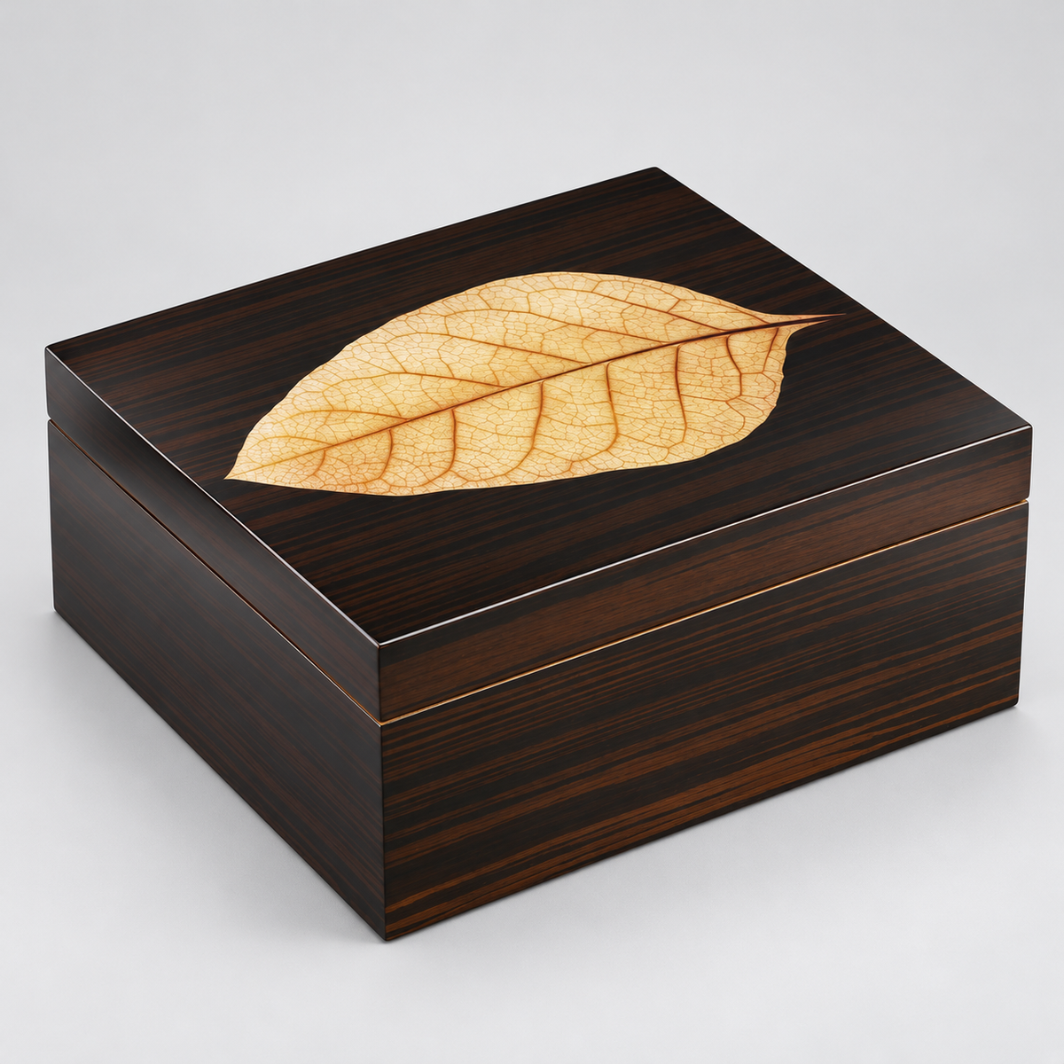 A square dark wood presentation box with a glossy finish, featuring an inlaid dried leaf on the lid, set against a neutral light gray background.