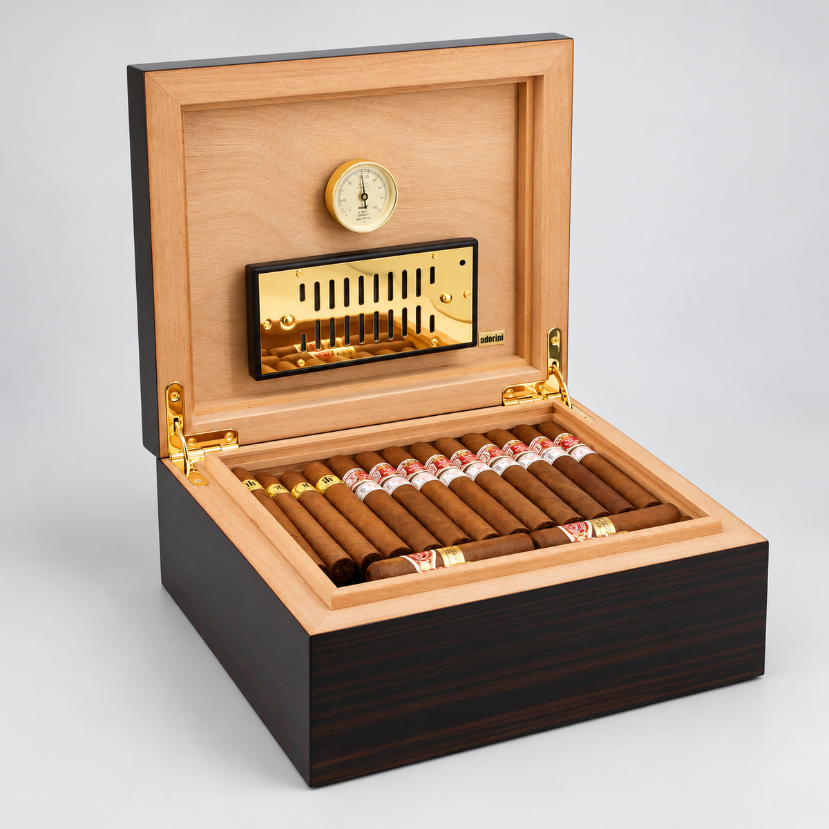 An open premium humidor box with a dark wood exterior, light wood interior, gold-tone hardware, a hygrometer, and a row of cigars inside, photographed on a light gray studio background.