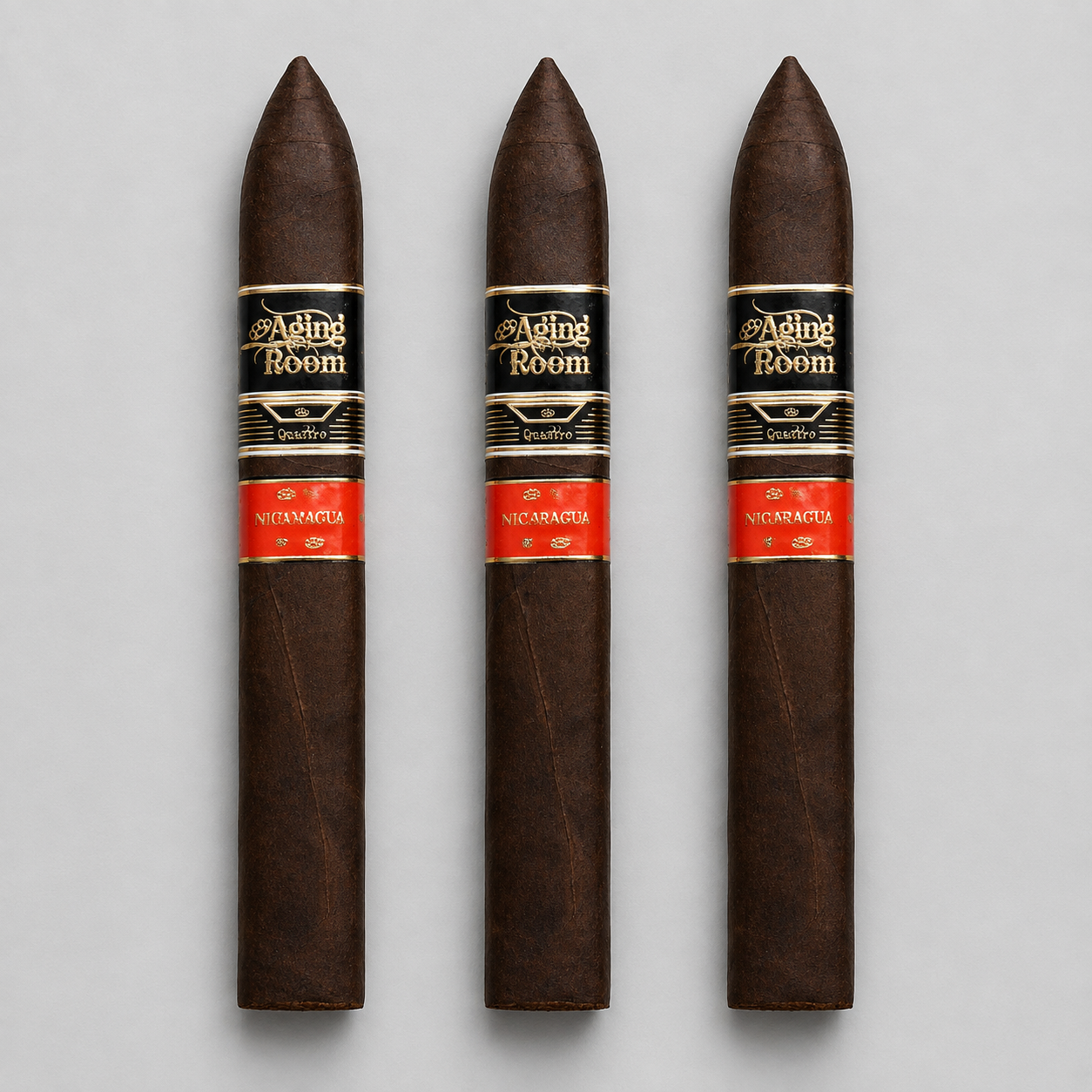 Three dark brown cigars with black and red bands labeled 'Aging Room' and 'Nicaraguan', arranged vertically on a light gray background.