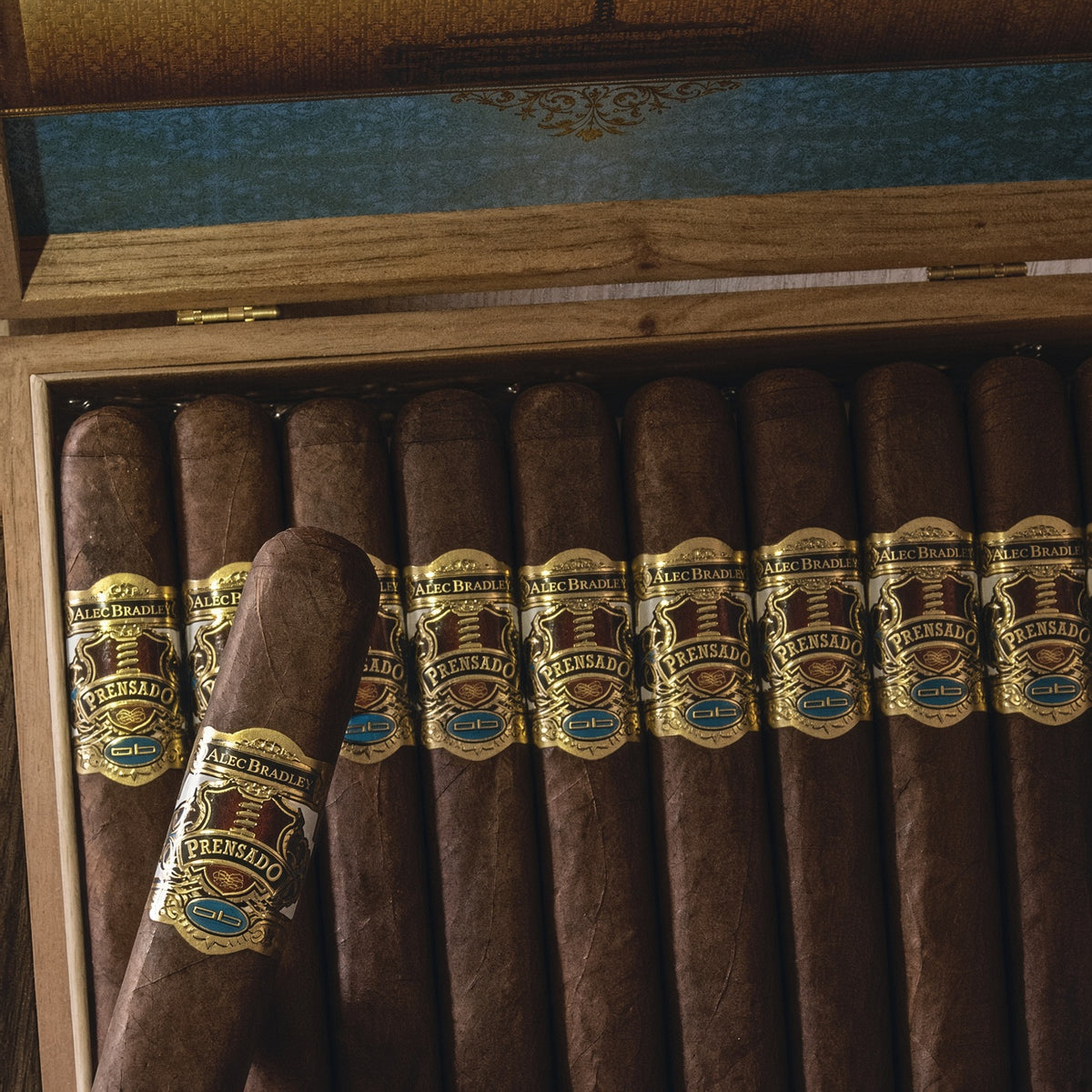 A close-up of a wooden cigar box filled with dark brown cigars. One cigar in the front has a prominent gold, brown, and blue band labeled 'A.