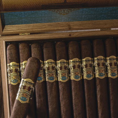 A close-up of a wooden cigar box filled with dark brown cigars. One cigar in the front has a prominent gold, brown, and blue band labeled 'A.