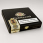 A black cigar humidor box by Prensado, featuring gold and white decorative branding, a gold clasp, and a prominent white smoking-health warning label on the front, photographed on a light gray background.