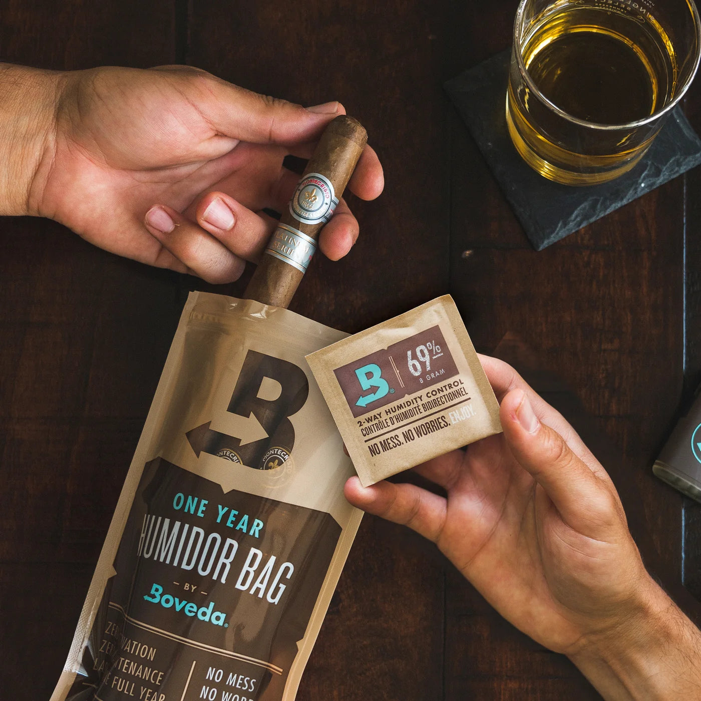 Person holding a Boveda one-year humidifier bag and a small Boveda packet on a wooden surface with a glass of beer.