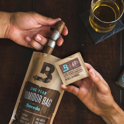 Person holding a Boveda one-year humidifier bag and a small Boveda packet on a wooden surface with a glass of beer.
