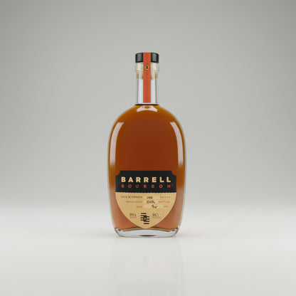 A bottle of Barrel Gold Whiskey with a small filled whiskey glass on a light beige surface.