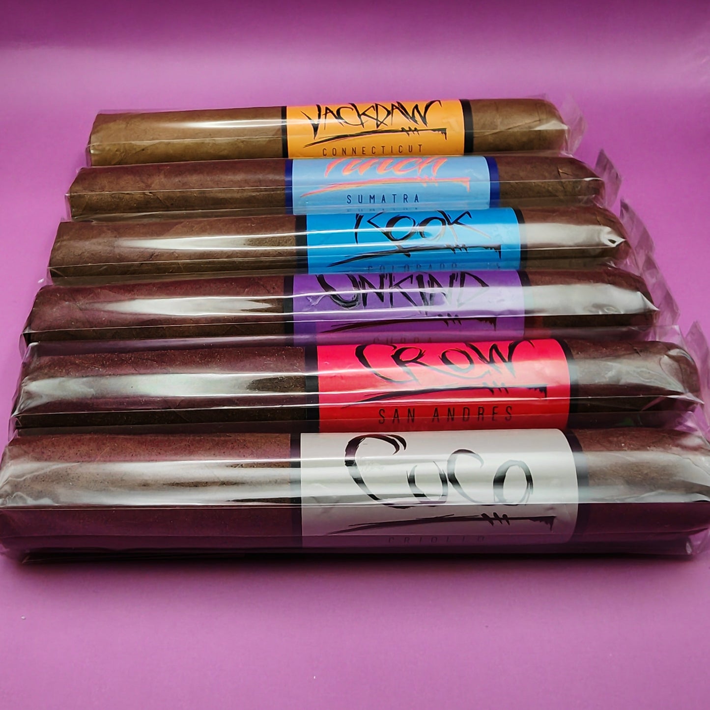 Packaged cigars with various brand labels on a pink background
