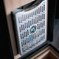 Close-up of a Boveda metal bracket device with a grid pattern and a Boveda logo on a wooden surface