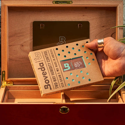 Hand holding a Boveda humidity control pack over an open wooden humidor.