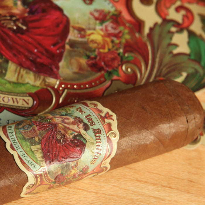 A close-up of a brown cigar with a colorful vintage-style label reading 'Sun Grown' and 'Cigarillo', resting on a light wood surface next to a matching branded wrapper roll.