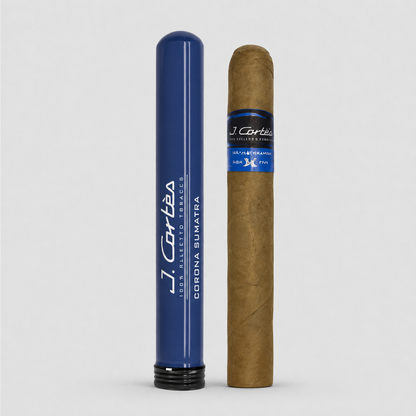 A single brown cigar stands next to a blue cylindrical holder with white text reading J. Cartéa and Corona Sumatra, on a light gray background.