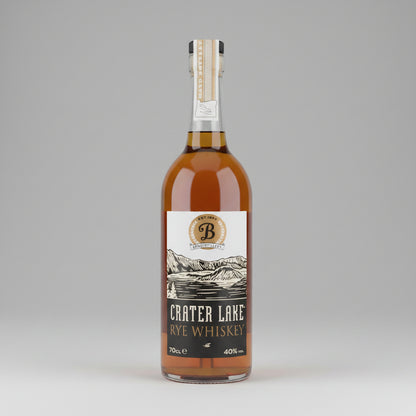 A bottle of Crater Lake Handcrafted American Rye Whiskey, showing the amber liquid inside a clear glass bottle with a white and black label.