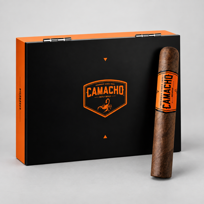 A Camacho cigar box in matte black with bright orange accents, shown open with one Camacho cigar standing upright in front on a light gray studio background.