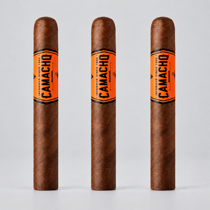Three Camacho Original cigars standing upright against a light gray background, each with a bright orange band featuring black text.
