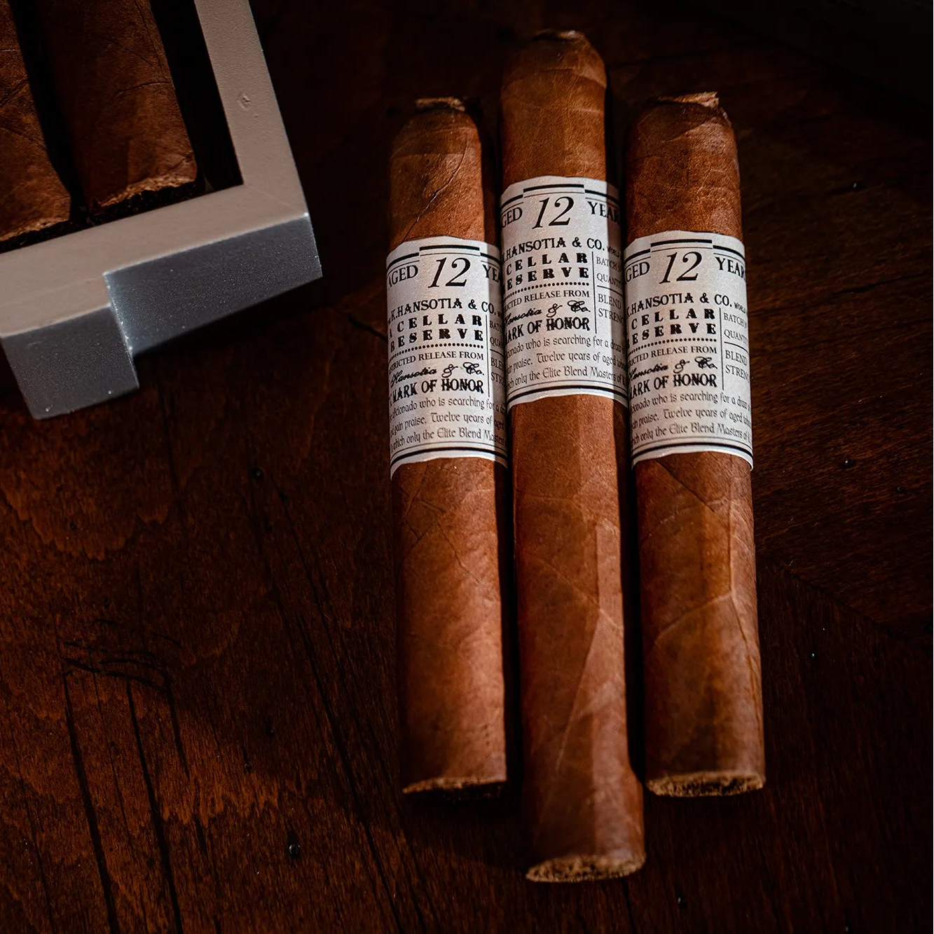 Three cigars with labels on a wooden surface, one of which is partially in a humidor.