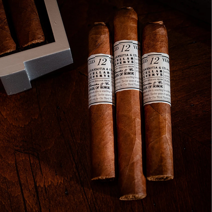 Three cigars with labels on a wooden surface, one of which is partially in a humidor.