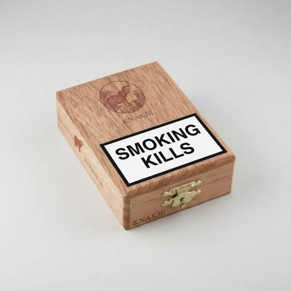 A wooden cigar box with a prominent white 'SMOKING KILLS' warning label on the lid, photographed on a neutral light gray background.