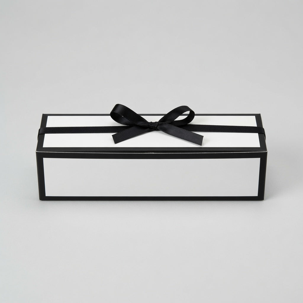 A rectangular gift box with a black frame and white interior, tied with a black satin ribbon and bow, photographed on a light gray studio background.